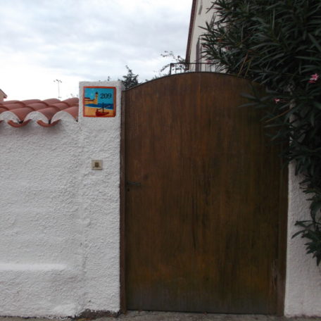 Plaque numéro de maison avec paysage marin et barque catalane verte, sur façade maison